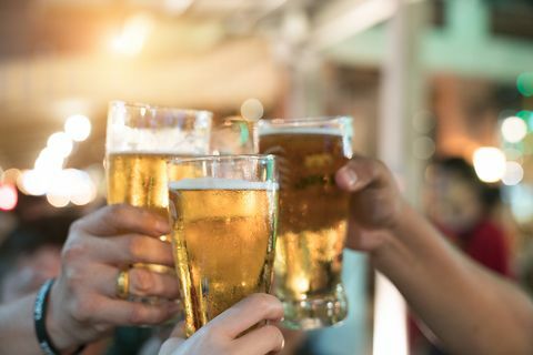 Vrienden die met glazen licht bier in de bar roosteren. Mooie achtergrond van het Oktoberfest. Een groep jongeren terwijl u ontspant aan de bar. fijne korrel. Zachte focus. Ondiepe DOF.