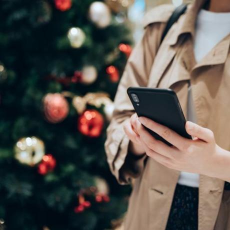 bijgesneden opname en middengedeelte van vrouw die smartphone gebruikt voor een kleurrijke kerstboom in het feestelijke kerstseizoen