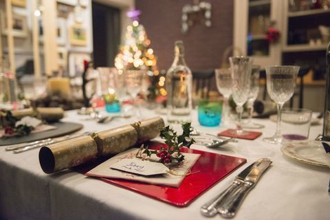 Een tafel gedekt voor een kerstmaaltijd, met zilveren en kristallen glazen en een kerstboom op de achtergrond.