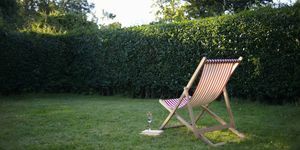 Een ligstoel met een boek en mousserende wijn, gelegen in een landelijke tuin.