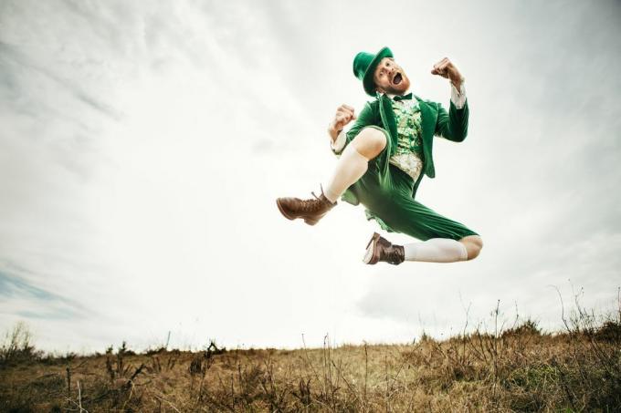 een stereotiep Iers personage helemaal klaar voor Saint Patrick's Day springt en danst in een open veld van Iers platteland kopieer ruimte in de lucht en gras