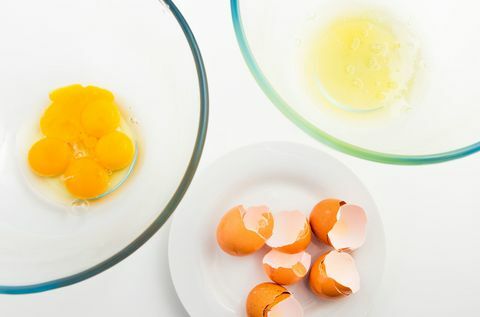 Eierdooier en eiwit in afzonderlijke glazen kom. Eierschaal en ei op witte plaat.