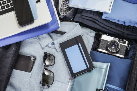 Luchtdetail van ingepakte koffer met blauw overhemd, retro camera, laptop, smartphone en notitieboekje