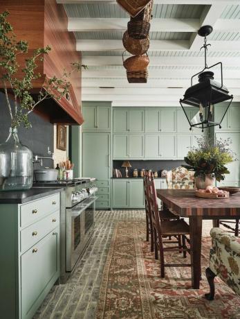keuken, groene kasten, vloerkleed, houten eettafel met houten stoelen, houten afzuigkap, groen
