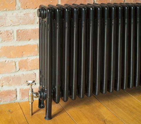 Zwarte radiator tegen bakstenen muur