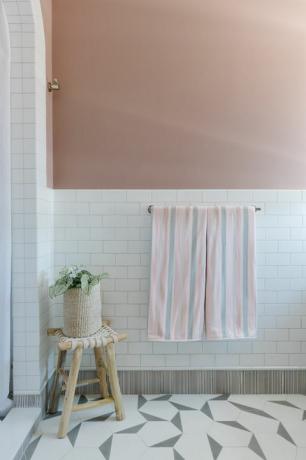 roze geschilderde muur, witte metrotegel, houten kruk, wit douchegordijn, geometrische witte en grijze tegels, roze en grijze handdoeken
