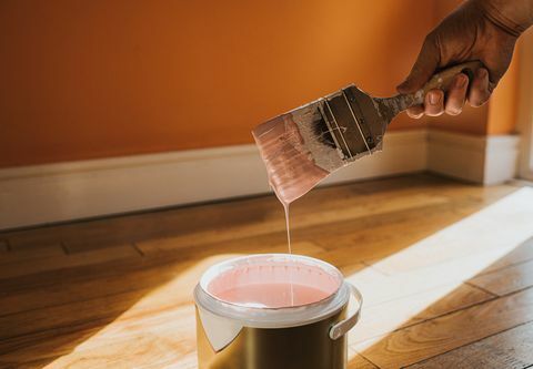hand houdt een dikke kwast vast en verwijdert deze, nadat deze in de verf is gedompeld, ontstaat er een druppel verf die spettert terug in de pot is de muur erachter oranje geschilderd en de kleur in het blik roze, wat conceptueel botst met ruimte voor kopiëren