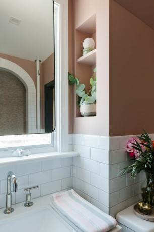witte metrotegels, roze geverfde muren, zilveren kraan, spiegel, ingebouwde planken, roze en grijze handdoeken
