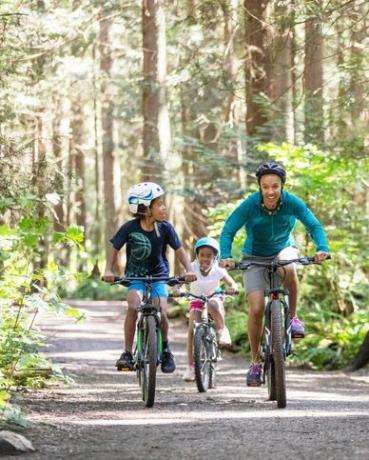 een vrouw en haar twee kinderen fietsen in het bos in de zon