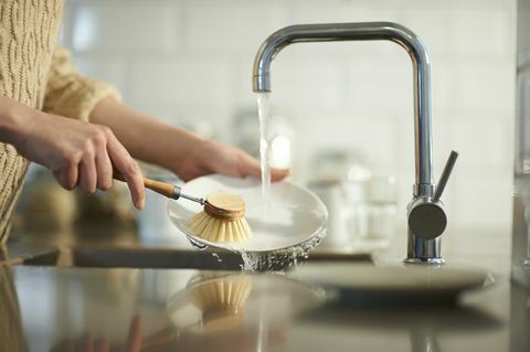 een vrouw gebruikt een plasticvrije borstel om de vaat in een aanrecht schoon te maken, close-up