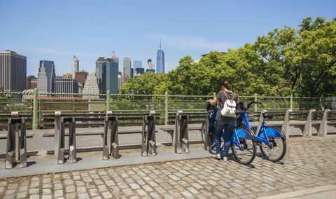 Vrouw die een fiets voor de horizon van Manhattan in de Stad van New York neemt