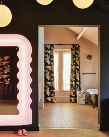 en suite badkamerbijpassende gordijnen, een open deuropening en een gedempte karamelkleurenschema verbinden de twee kamers spiegel vintage ettore sottsass tegels winckelmans