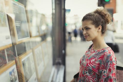 Jonge vrouw die onroerende goederenlijsten doorbladeren bij stedelijke storefront