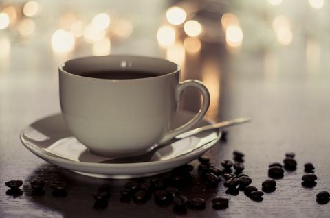 Kop en schotel met koffie zat op een tafel vol met koffiebonen.