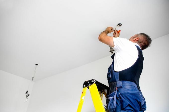 een reparateur, een mannelijke elektricien, repareert het licht en installeert led-verlichting in een plafondarmatuur
