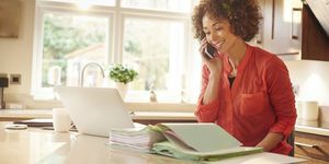 Vrouw zit in haar keuken en werkt wat papierwerk tijdens het chatten aan de telefoon