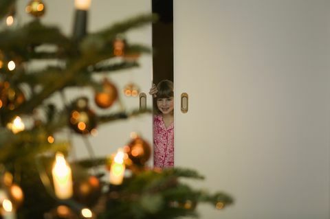 Meisje in pyjama's die door deur bij Kerstboom turen
