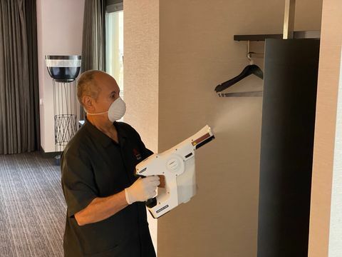 man in een hotelkamer met behulp van een sproeier om open kast te desinfecteren