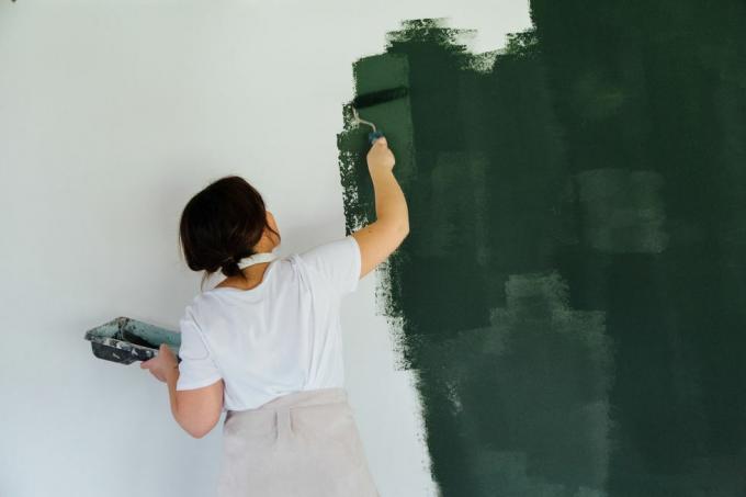 vrouw in hoofdtelefoons die witte muur in groene kleur schilderen