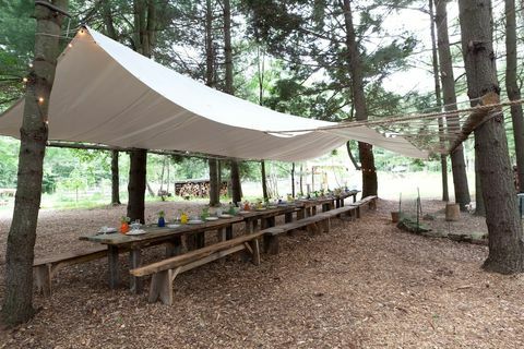 eethoek met houten tafels en banken, tented met zeildoekachtig materiaal bevestigd aan bomen langs de eethoek